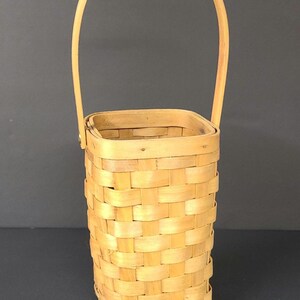 Peut inclure: Un panier en osier tressé avec une base carrée et une seule poignée. Le panier est fait d'osier brun clair naturel.