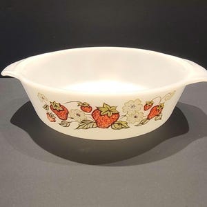 May include: White, oval serving bowl with two handles. The bowl has a decorative pattern of red strawberries, green leaves, and white flowers around the rim. The bowl is made of a durable, opaque material.