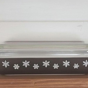 May include: A brown glass baking dish with a clear glass lid. The dish features a snowflake design on the front.