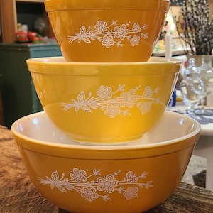 May include: A set of three yellow mixing bowls with a white floral design. The bowls are nested inside each other.