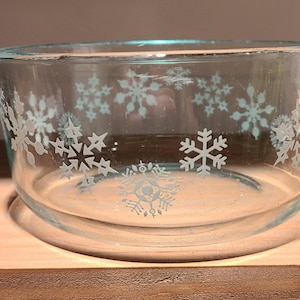 May include: A clear glass bowl with a snowflake design. The bowl is sitting on a wooden surface.