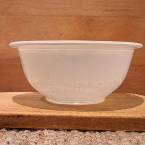 May include: A white ceramic bowl with a slightly textured surface. The bowl is empty and appears to be used.