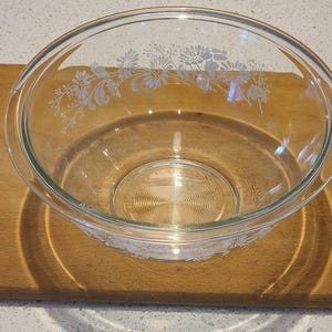 May include: A clear glass mixing bowl with a floral design etched into the side. The bowl is sitting on a wooden surface.