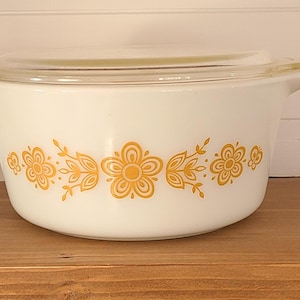 May include: White casserole dish with a glass lid and a yellow floral pattern around the rim.