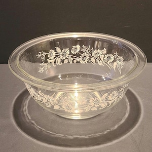 May include: A clear glass mixing bowl with a white floral design. The bowl has a wide rim and a rounded bottom.