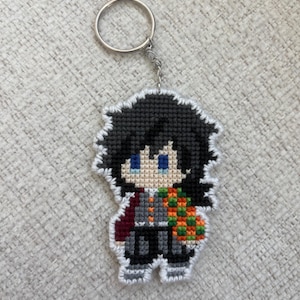 May include: A handmade keychain featuring a pixelated anime character with black hair, blue eyes, and a patterned haori. The keychain is made of stitched plastic canvas and includes a silver keyring and chain.