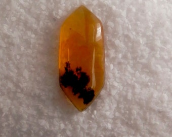 May include: A yellow and black agate cabochon with a pointed shape. The agate has a dendritic pattern.