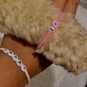 May include: A white string bracelet with the word "ZARA" and a pink heart charm. A pink string bracelet with the letter "Z" and a pink heart charm.