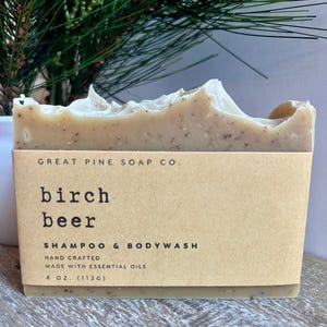 May include: A bar of handmade birch beer shampoo and bodywash from Great Pine Soap Co. The soap is light brown with visible flecks and is wrapped in a tan paper label. The label reads "birch beer" and "4 oz. (113g)".
