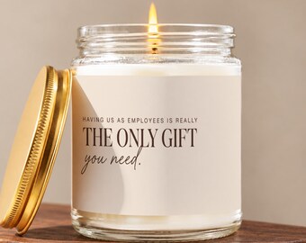 May include: A clear glass candle jar with a gold-colored metal lid placed to the side. The candle features a white label with the black text: HAVING US AS EMPLOYEES IS REALLY THE ONLY GIFT you need. The candle is lit with a visible flame.