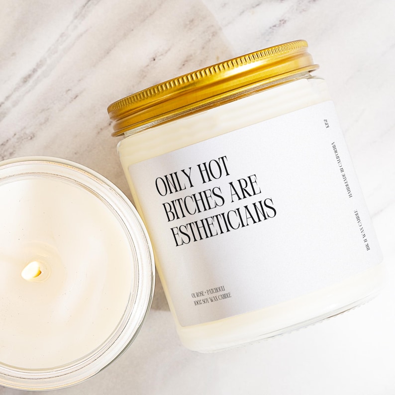 A white candle with a gold lid, and a small candle in the background, both placed on a marble surface.