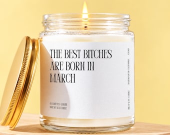 May include: A clear glass jar candle with a gold lid and a white label featuring the black text THE BEST BITCHES ARE BORN IN MARCH, 08 WHITE TEA + JASMINE, 100% SOY WAX CANDLE, HANDMADE IN CALIFORNIA, and KZ008. The candle has a lit wick.