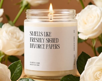May include: A lit soy wax candle in a clear glass jar with a gold lid. The white label features black text reading: SMELLS LIKE FRESHLY SIGNED DIVORCE PAPERS, OR WHITE TEA + JASMINE, 100% SOY WAX CANDLE, HANDMADE IN CALIFORNIA, K221.