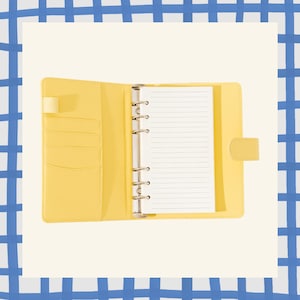 May include: Open yellow binder with lined paper. The binder has a tab closure and several pockets on the left side. The binder is open, revealing the lined pages and metal rings.