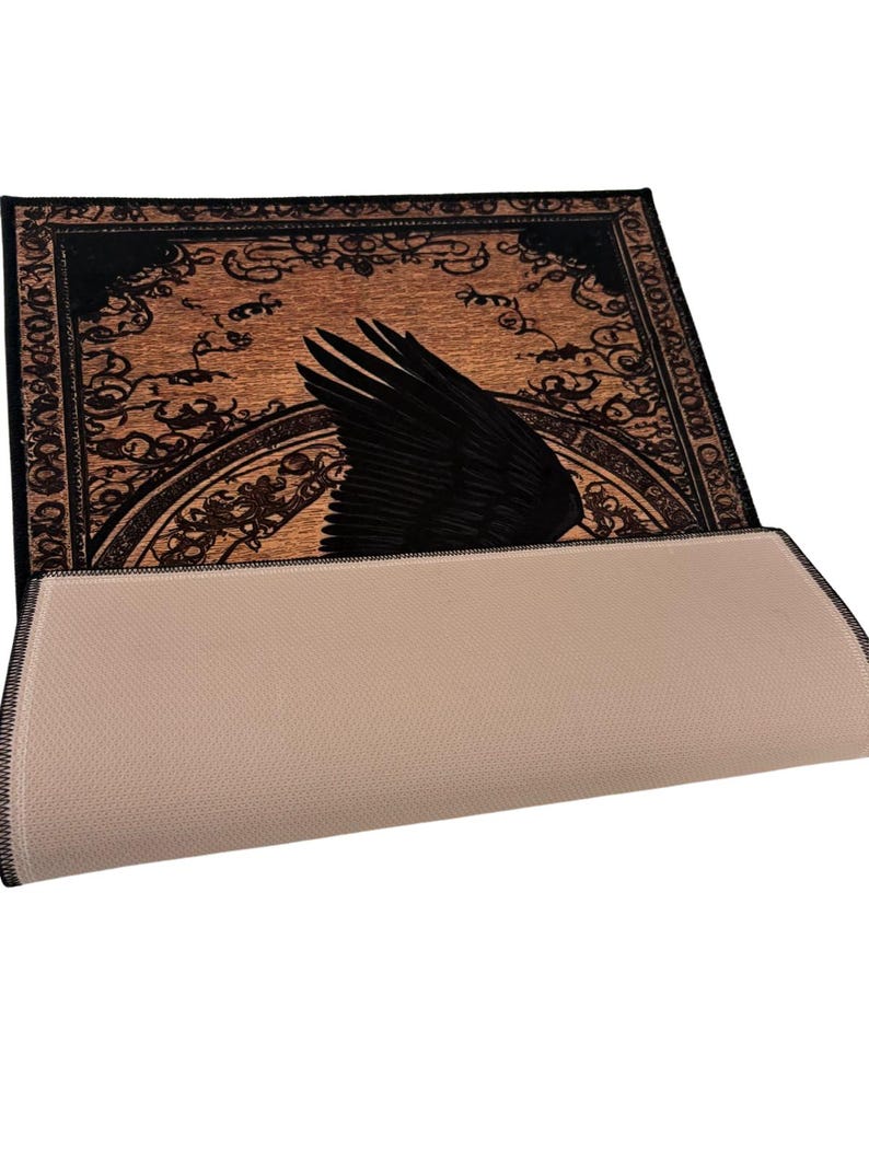 May include: A rectangular rug with a black raven wing design on a brown background. The wing is prominently displayed against a backdrop of ornate, swirling patterns. The rug's underside is a light beige color.