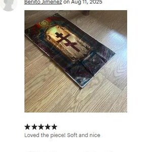 May include: A rectangular, religious-themed artwork featuring a central cross design. The artwork has a gold and brown color scheme with a dark border. The image is on a wooden floor.