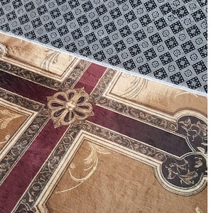 May include: A decorative rug with a cross-shaped design in shades of brown, burgundy, and gold. The rug features an ornate floral pattern in the center and along the edges. The top portion of the rug has a black and white geometric pattern. The word "SAMPLE" is in a red rectangle.