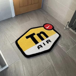 May include: A yellow and white doormat with a black outline and the text "Tn AIR" in black lettering. A red circle with a white Nike swoosh is in the upper right corner.