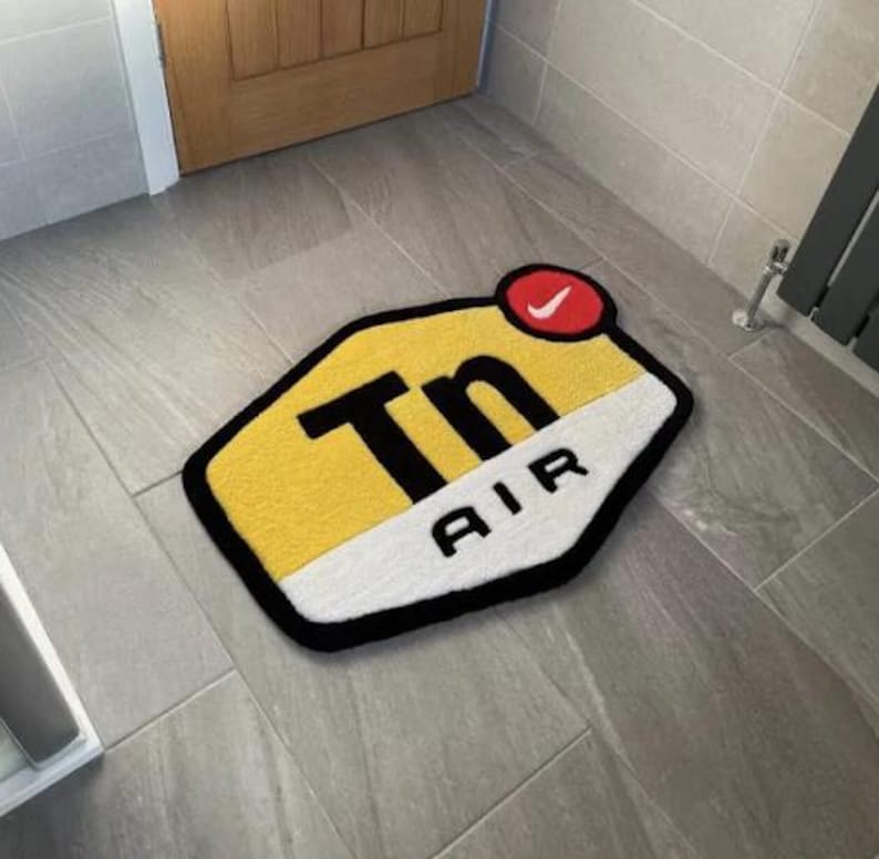 May include: A yellow and white doormat with a black outline and the text "Tn AIR" in black lettering. A red circle with a white Nike swoosh is in the upper right corner.
