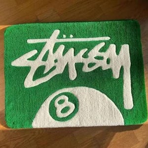 May include: Green doormat with a white 8-ball and the word "STUSSY" in white lettering.
