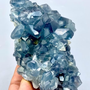 May include: A cluster of blue celestite crystals with a glassy, translucent appearance. The crystals are arranged in a random, organic pattern, creating a visually appealing and unique piece.