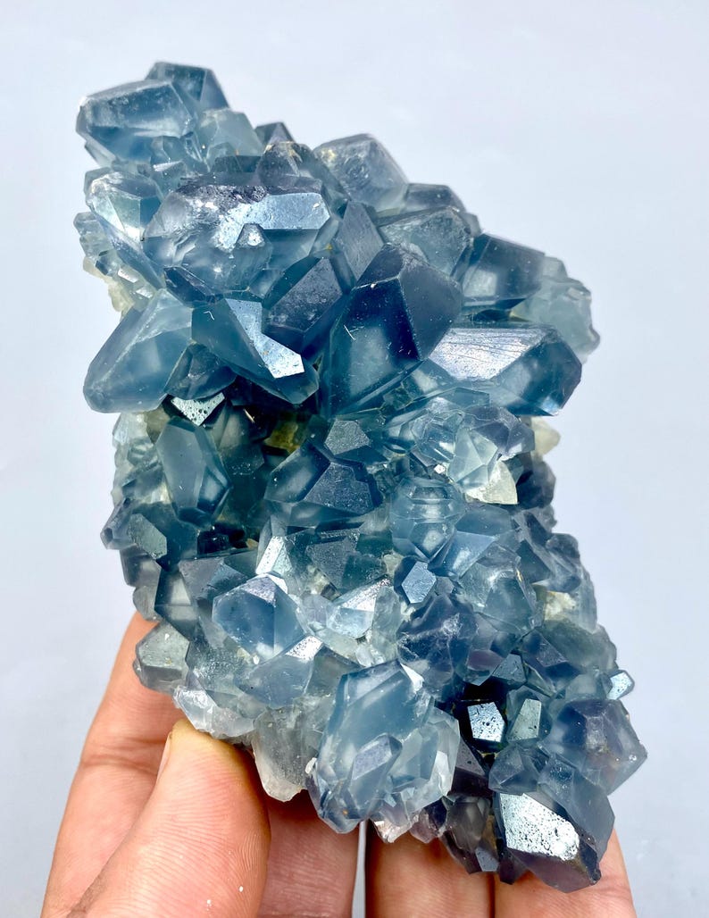 May include: A cluster of blue celestite crystals with a glassy, translucent appearance. The crystals are arranged in a random, organic pattern, creating a visually appealing and unique piece.