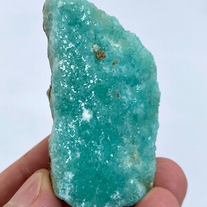 May include: A teal green, rough-cut, crystal with a sparkly, iridescent surface. The crystal has a unique, irregular shape.