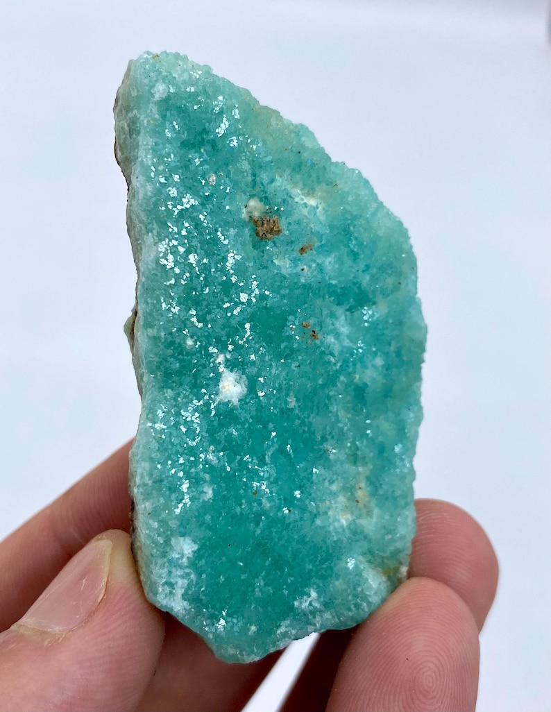 May include: A teal green, rough-cut, crystal with a sparkly, iridescent surface. The crystal has a unique, irregular shape.
