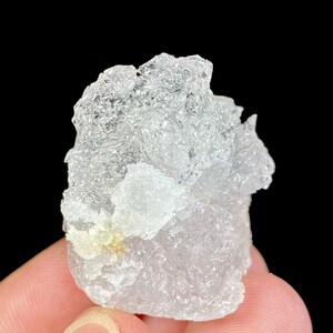 Può includere: Un gruppo di cristalli di quarzo trasparenti, traslucidi e leggermente opachi con un piccolo cristallo giallo-verde al centro.