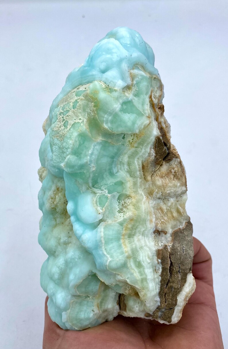 May include: A large, blue and green, naturally formed,  crystal cluster with a rough, brown exterior.