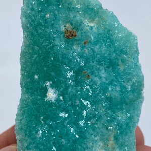 May include: A large, teal green, rough-textured, crystal specimen with white and brown inclusions.