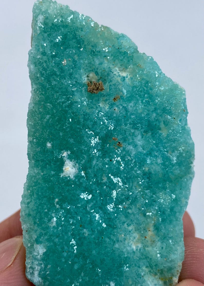 May include: A large, teal green, rough-textured, crystal specimen with white and brown inclusions.