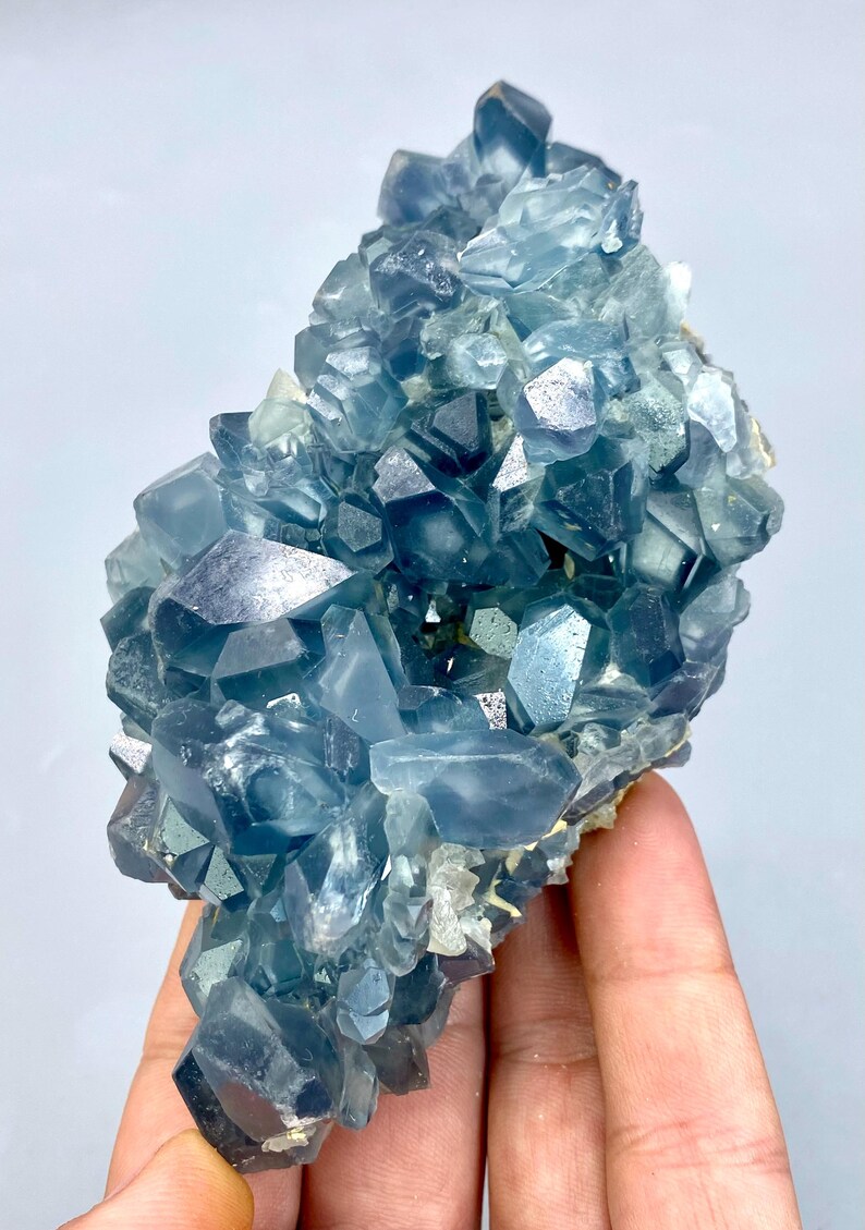 May include: A cluster of blue celestite crystals with a glassy, translucent appearance. The crystals are arranged in a random, organic pattern, creating a visually appealing and unique piece.