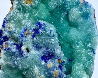 May include: A close-up of a mineral specimen featuring a mix of colors. The dominant hues are shades of teal and blue, with areas of crystalline texture. There are also patches of brown and yellow. The overall appearance suggests a natural, geological formation.
