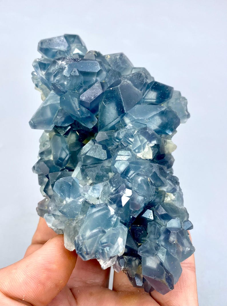 May include: A cluster of blue celestite crystals with a variety of sizes and shapes. The crystals are translucent and have a slight shimmer.