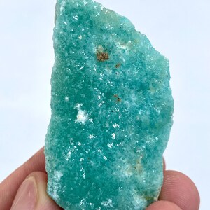 May include: A large, rough, green, and white, natural, raw, uncut, crystal of amazonite. The crystal has a smooth, polished surface and is a light, translucent green color.