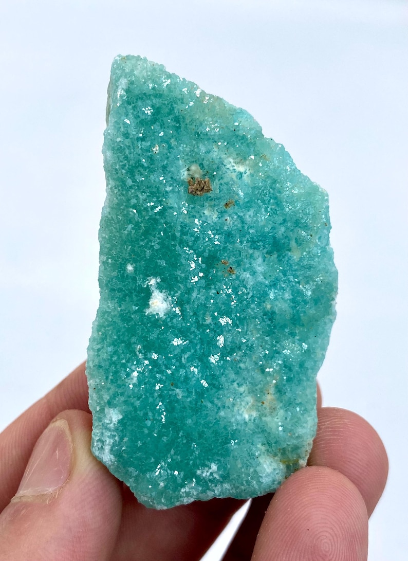 May include: A large, rough, green, and white, natural, raw, uncut, crystal of amazonite. The crystal has a smooth, polished surface and is a light, translucent green color.