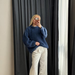 May include: A woman wearing a dark blue, oversized sweater and white wide-leg pants. The sweater has a crew neck and long sleeves. The pants are high-waisted and have a pleated front. The outfit is being reflected in a large mirror.