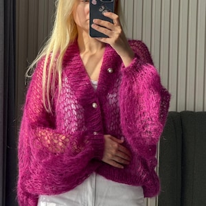 Puede incluir: Un cárdigan fucsia vibrante con un delicado diseño de punto calado. El suéter de manga larga presenta un cuello en V y se abrocha con tres botones perlados. La textura esponjosa y el color brillante lo convierten en una pieza llamativa.