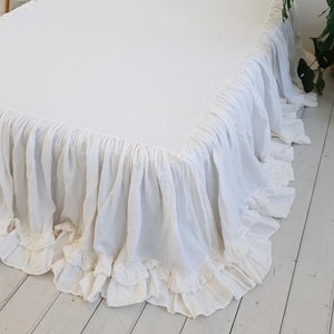 May include: A white bed skirt with a ruffled design. The bed skirt is made of a soft, textured fabric and has a simple, elegant style. The bed skirt is designed to fit a standard bed frame.