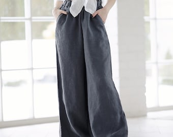 May include: A woman wearing a white linen shirt tied at the waist and wide-legged dark gray linen pants.
