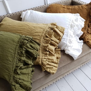 May include: Four pillowcases with ruffled edges in different colors: green, mustard yellow, white, and a darker mustard yellow. The pillowcases are arranged on a brown couch.