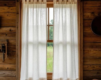 May include: Sheer white linen curtains hanging in a wooden window frame. The curtains are semi-transparent, allowing natural light to filter through. The window is set in a rustic, wood-paneled wall, creating a cozy, farmhouse aesthetic.