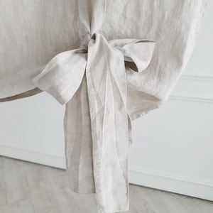 May include: A close-up of a light beige linen fabric tied into a bow. The fabric is soft and has a natural texture.