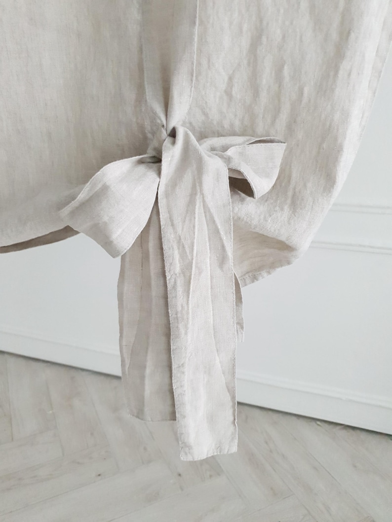 May include: A close-up of a light beige linen fabric tied into a bow. The fabric is soft and has a natural texture.