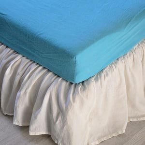 May include: A white bed skirt with a ruffled edge, layered over a light blue fitted sheet.