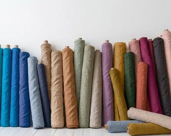 May include: A collection of fabric bolts arranged in a row, featuring a diverse spectrum of colors including shades of blue, green, yellow, purple, pink, brown, and beige. Each roll is tightly wound, displaying a textured, woven material surface.