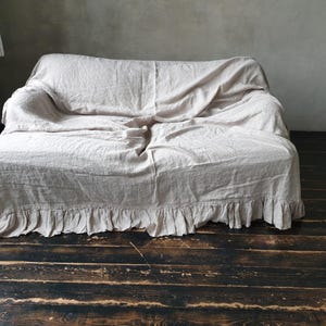 May include: A white linen sofa throw with a ruffled edge. The throw is draped over a sofa and has a relaxed, casual look.