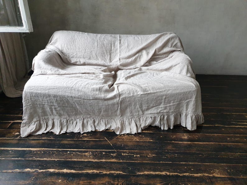 May include: A white linen sofa throw with a ruffled edge. The throw is draped over a sofa and has a relaxed, casual look.