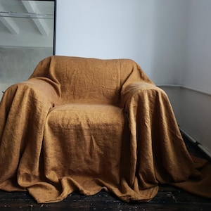 May include: A brown linen throw blanket draped over a chair. The blanket is a soft, natural color and has a textured weave.